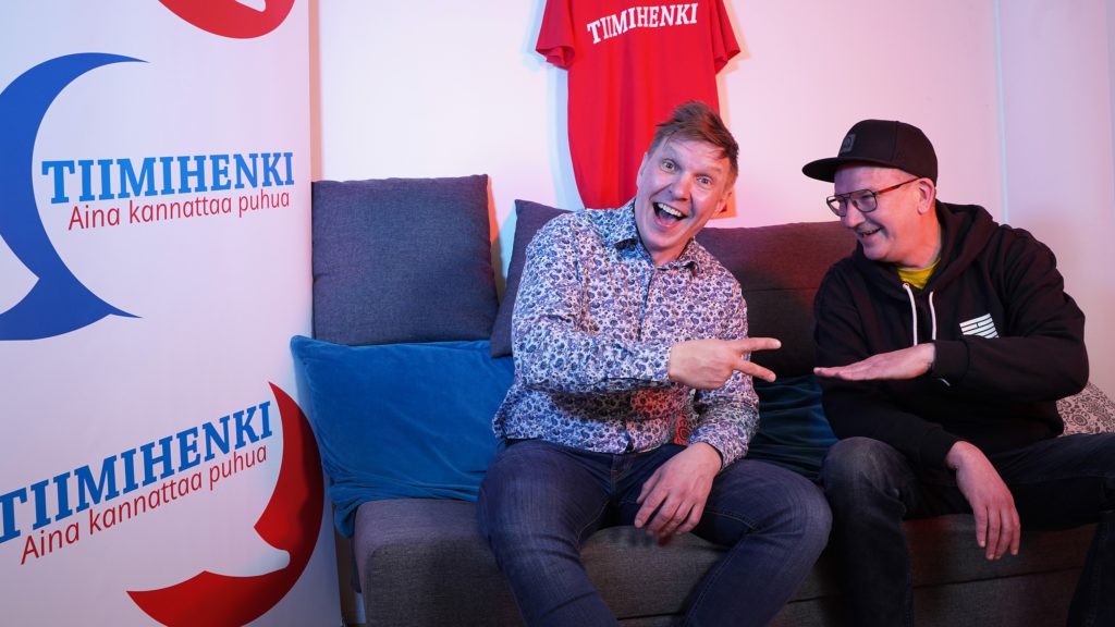 Sohvalla istuu kaksi miestä, Jukka-Tapio Keränen ja Janne Seppälä. He pelaavat kivi-paperi-sakset peliä ja nauravat.