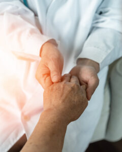 Kuvassa näkyvät kahden henkilön kädet. Valkoisessa takissa oleva henkilö pitelee toisen henkilön vasenta kättä.