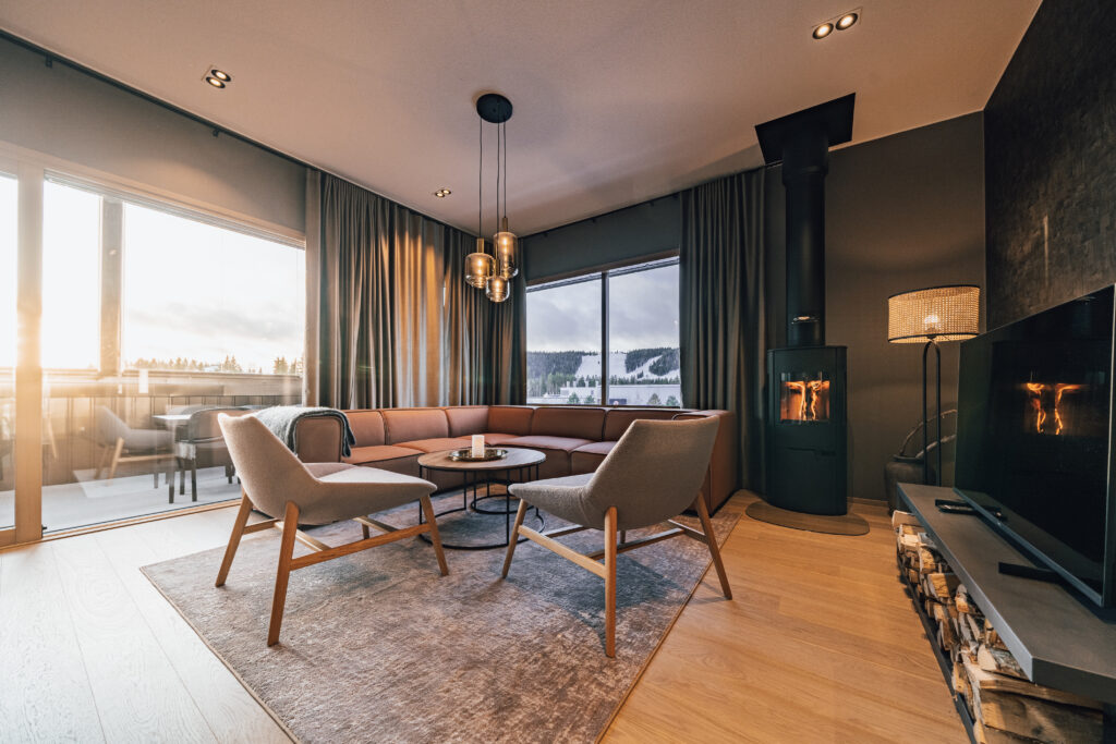 Kuvituskuva hotellihuoneesta. Moderni, valoisa huone, jossa ikkunat kahdella seinällä. Aurinko paistaa matalalta sisään huoneeseen ja luo lämpimän tunnelman.